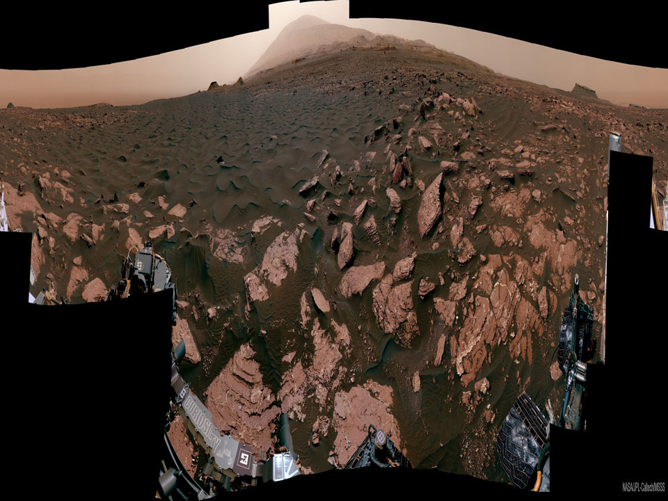 Rocks and brown sand occupy this horizontally compressed
image of Mars. At the top is a light coloured peak. 
Please see the explanation for more detailed information.