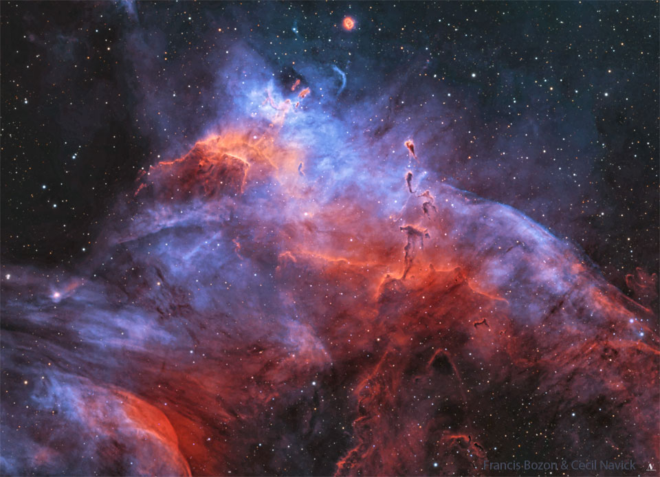 A starfield is shown dominated by a purple and red nebula.
Several dark dust pillars are visible that appear not unlike
tadpoles. 
Please see the explanation for more detailed information.
