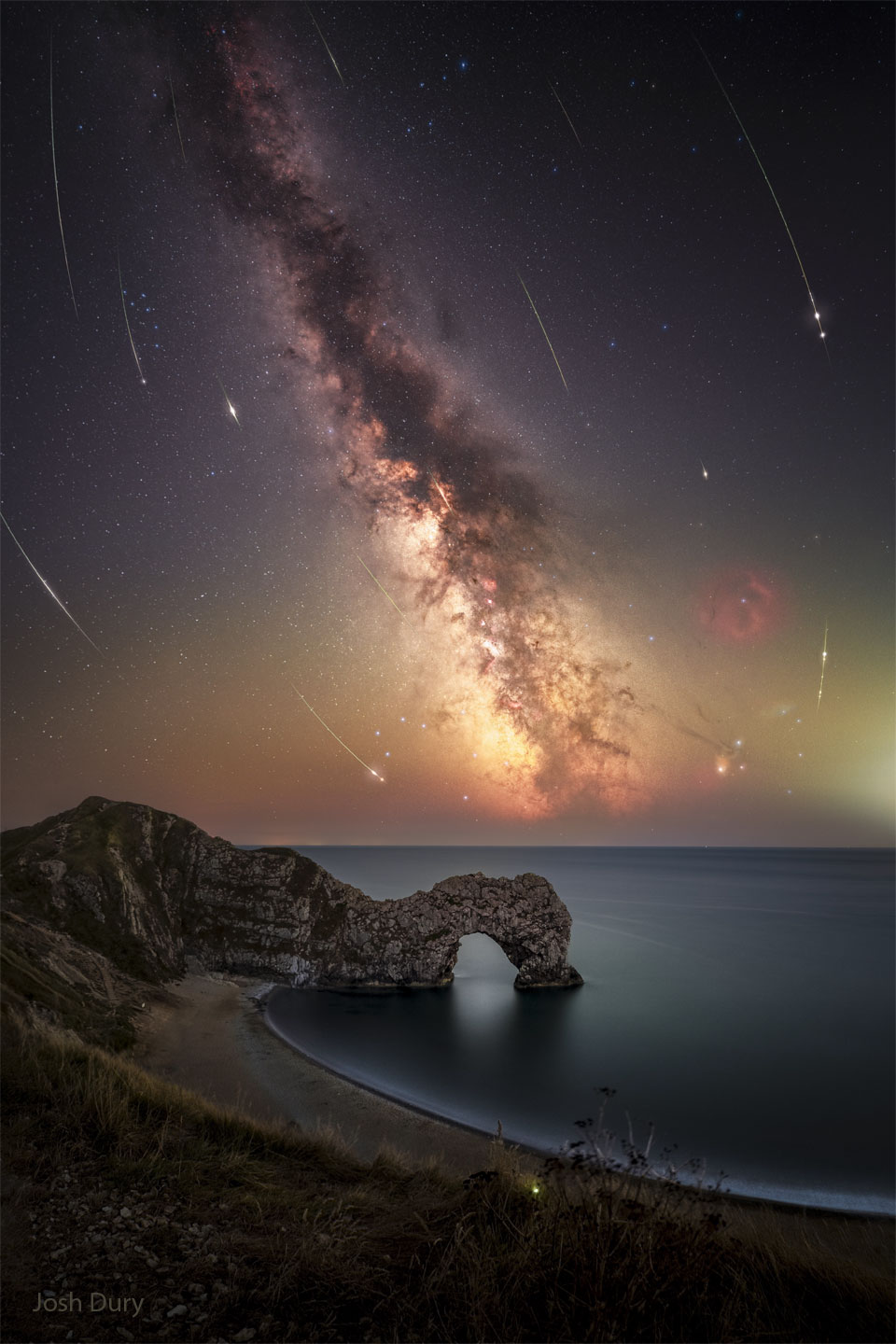 A deep sky is shown with the band of our Milky Way Galaxy
running from the upper left to the lower right. The streaks
or many curved meteors are seen. In the foreground a beach
is seen with an unusual rock outcrop that has an opening.
Please see the explanation for more detailed information.