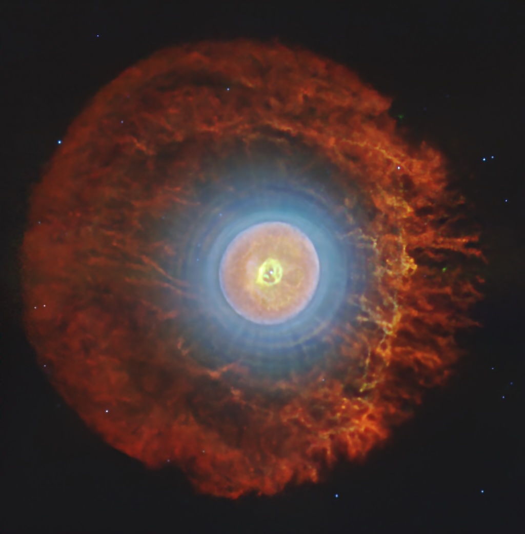 A spherical nebula shows concentric
	  rings of different colours over a dark
	  background with a few stars.
