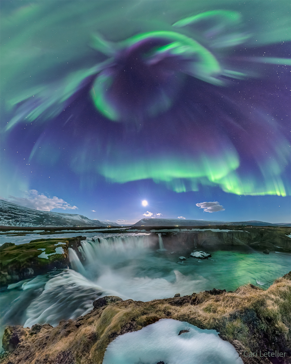 Green aurora are seen against a blue sky 
over a series of picturesque waterfalls.
Please see the explanation for more detailed information.