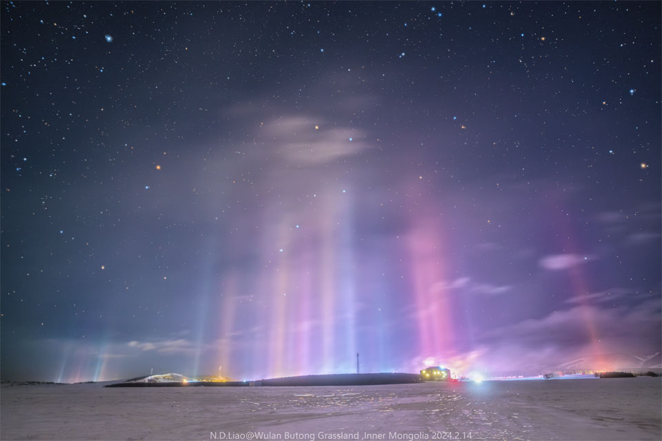 Numerous thin pillars of light connect a landscape filled
with snow to a star filled sky. The Big Dipper can be seen through
the colourful pillars.
Please see the explanation for more detailed information.