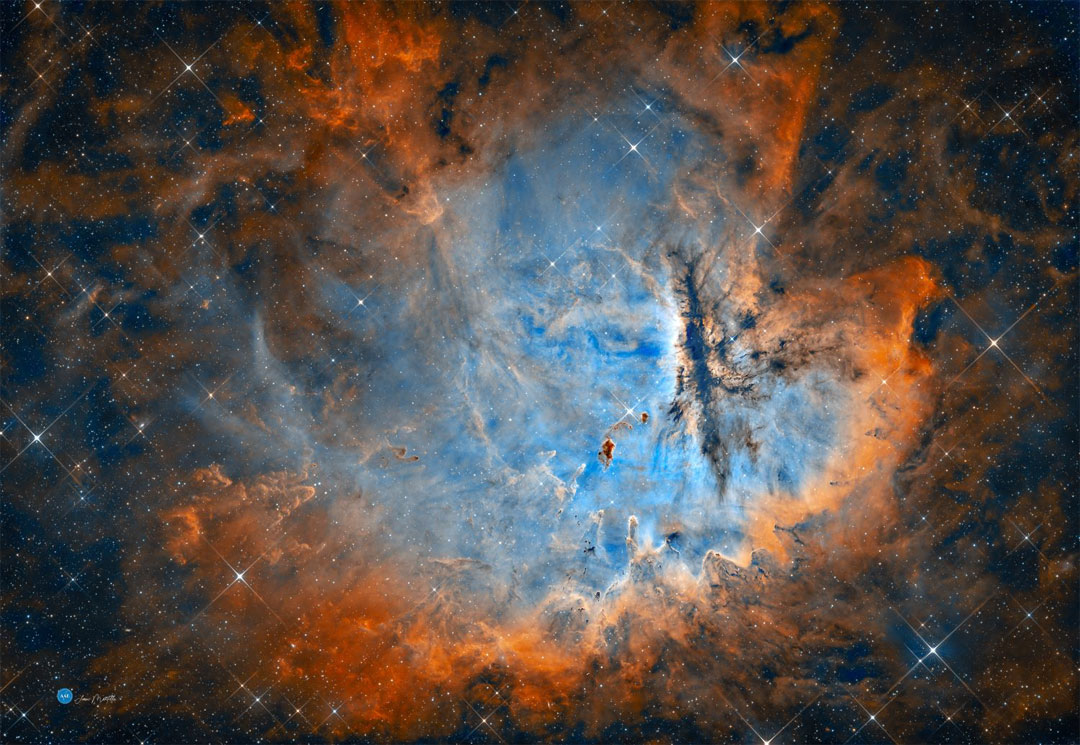 A starfield dominated by a large nebula is pictured. 
The centre is blue and the perimeter is red. Many dark 
dust pillars are visible. 
Please see the explanation for more detailed information.
