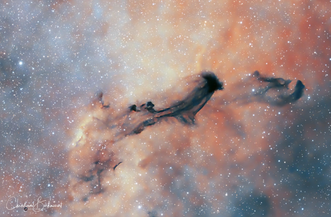 A starfield with a light, orange-tinged background 
has a dark nebula that looks like a flying ghost visible
near the middle. 
Please see the explanation for more detailed information.