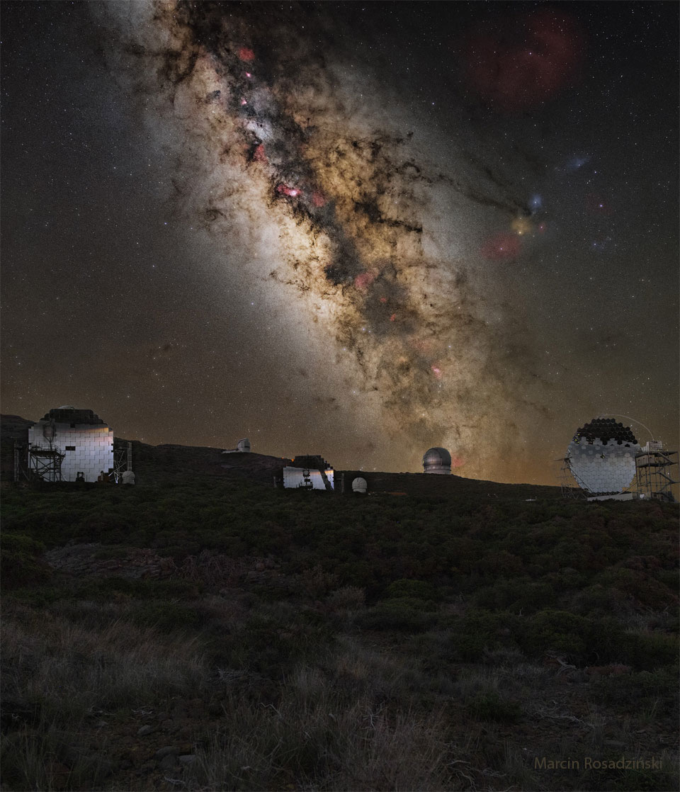 A mountaintop is shown covered by brush. Across the horizon are
several telescopes. Behind the mountaintop is a deep exposure of
the sky showing the central band of our Milky Way galaxy and several
well-known stars and nebulae.
Please see the explanation for more detailed information.