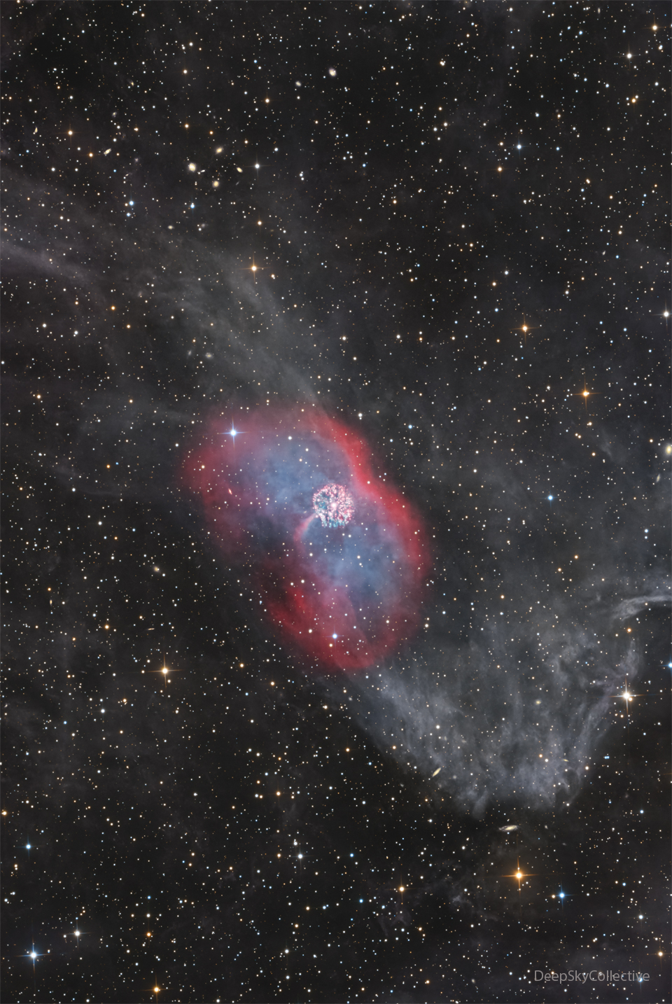 A faint nebula runs vertically in the image. In the
centre is a red envelope surrounding diffuse blue emission.
In the centre is a bright multicoloured nebula that is 
nearly circular. 
Please see the explanation for more detailed information.