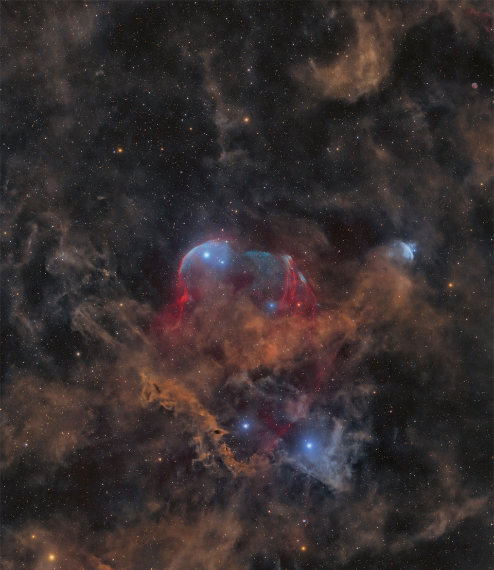A starfield is shown with many stars and several faint
light brown dust clouds. In the centre is a large cloud with
brown dust and gas shells lined in blue. 
Please see the explanation for more detailed information.