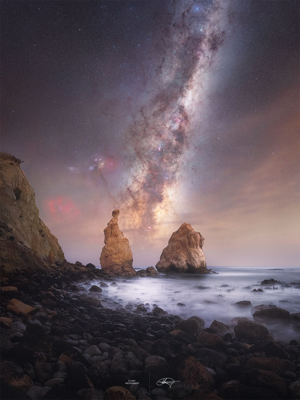 A skyscape is seen above an water inlet.
Two rock spires rise from the sea, and the central
band of our Milky Way Galaxy is seen between them.
Please see the explanation for more detailed information.