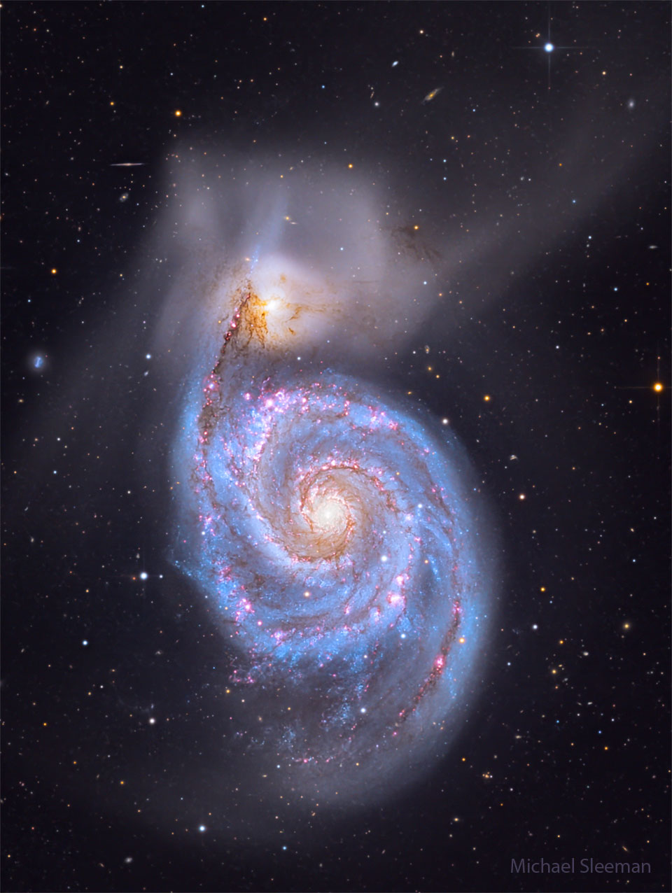 A big spiral galaxy fills the frame, complete with blue
spiral arms dotted with red dust and nebulae. Above the 
spiral galaxy is another more diffuse galaxy that has
faint wisps extending in many directions. 
Please see the explanation for more detailed information.